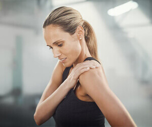 A woman in a black tank top holding onto her shoulder in pain. 