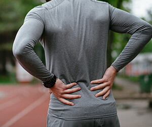 A man on a track holding his lower back due to his sacroiliac joint pain.